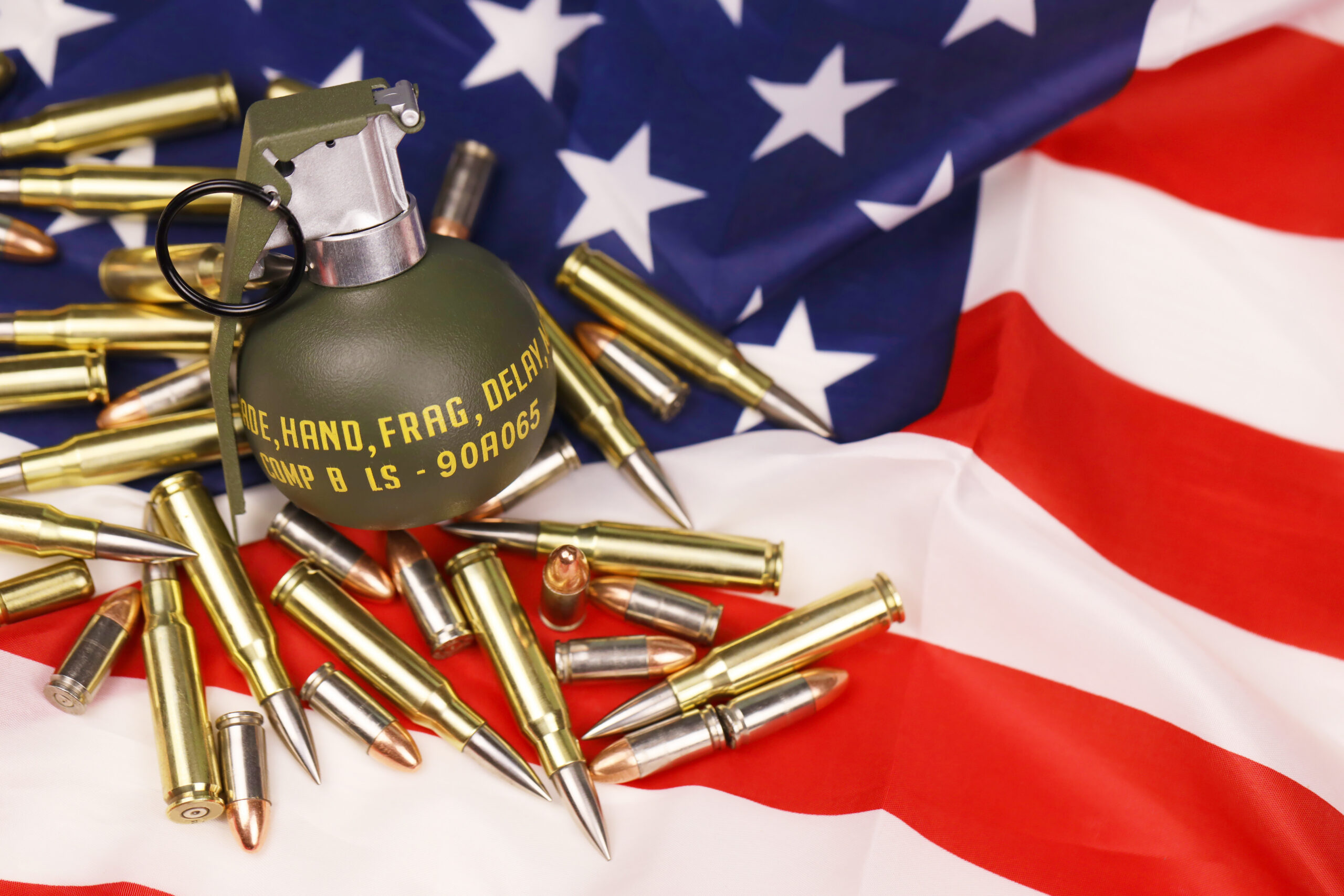 M67 frag grenade and many yellow bullets and cartridges on United States flag. Concept of gun trafficking on USA territory or special operations