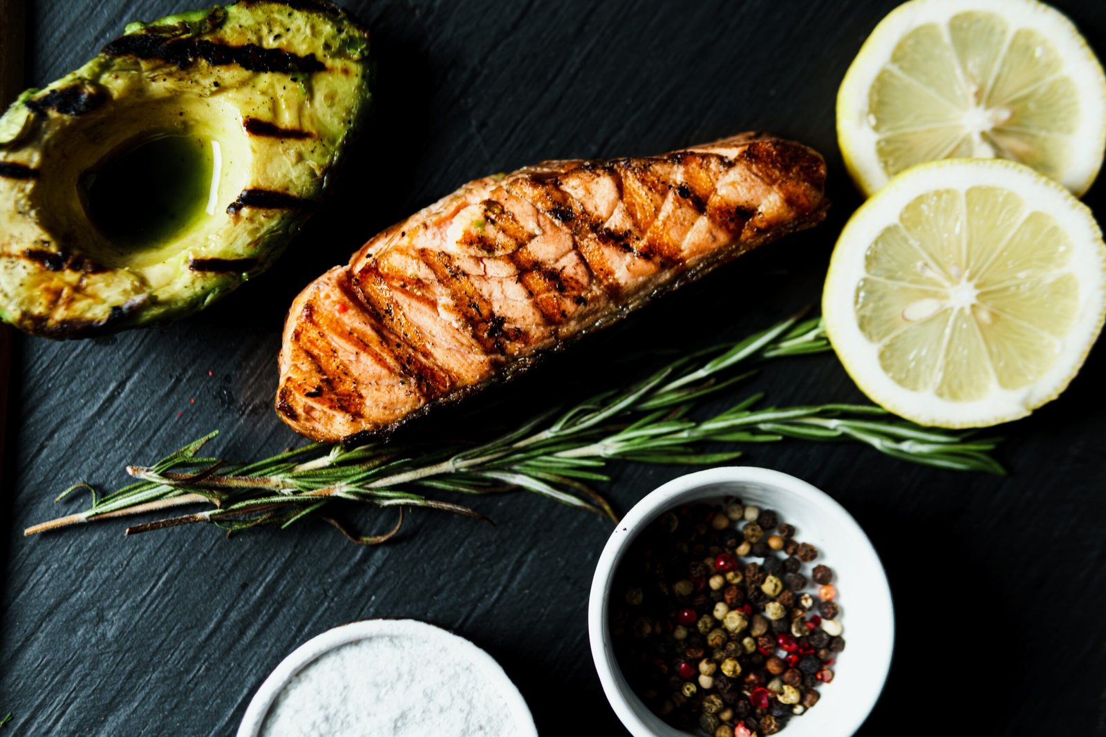 Grilled salmon fish fillet with green salad on the black cutting board, close up. Delicious food in the restaurant menu. Concept of catering service