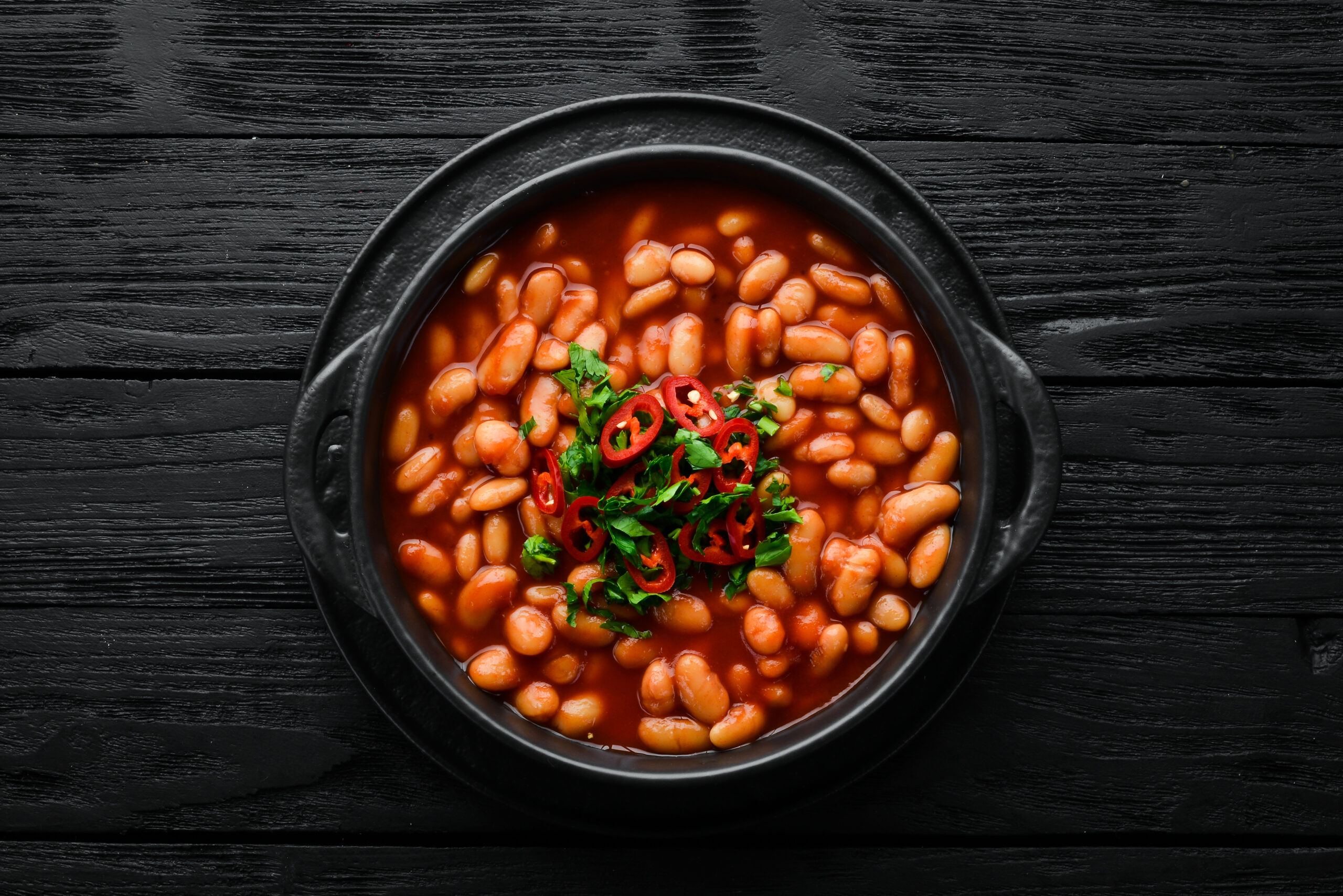 Vegetarian menu. Stewed beans in tomato sauce with parsley and chili. In a black bowl. Top view. Free space for your text.