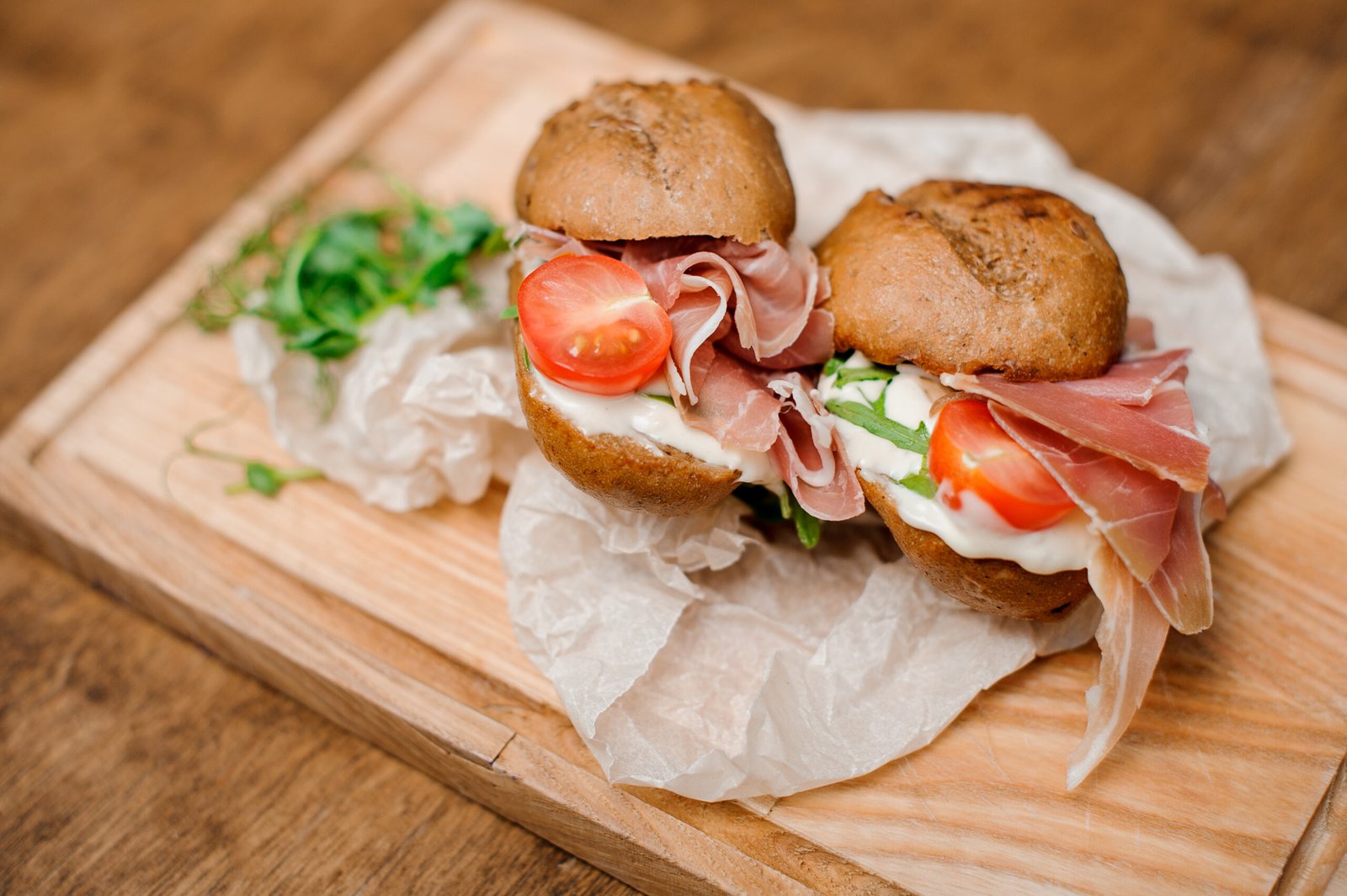 Two appetizing sandwitches with tasty ham, red tomatoes and creamy cheese serving on the wooden plato