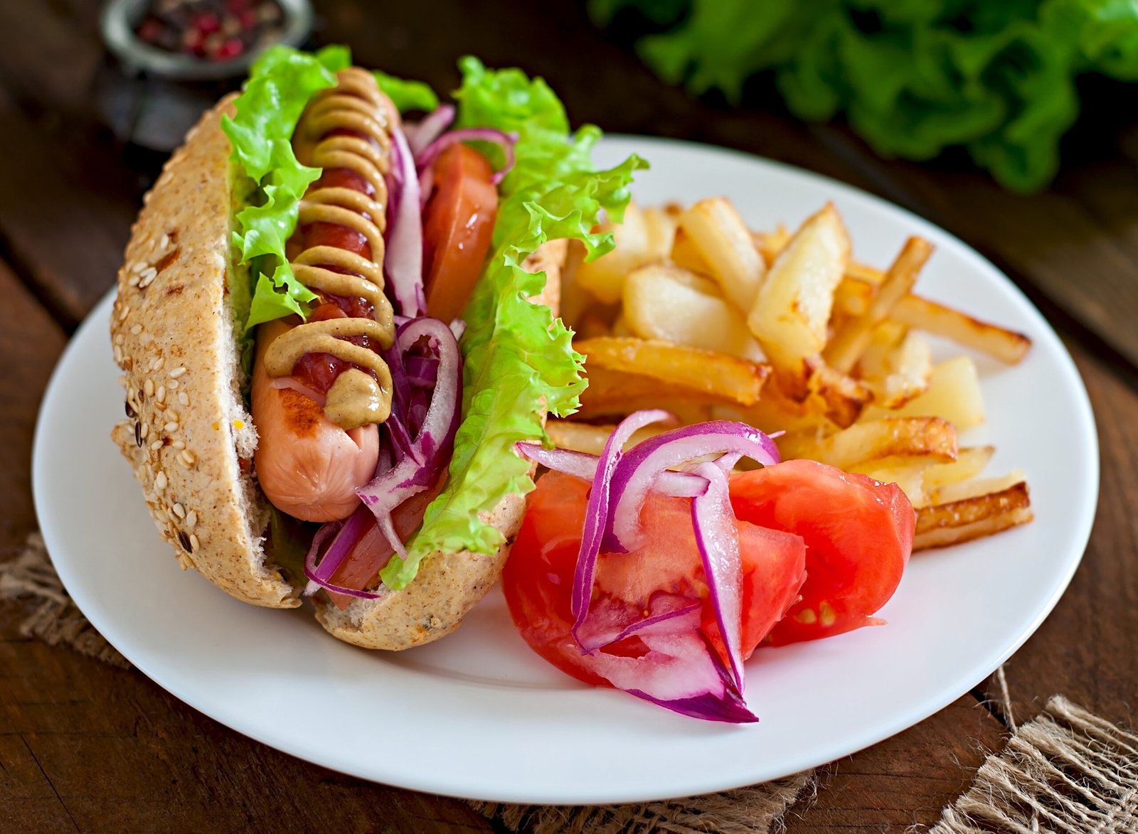 Hotdog with ketchup mustard and lettuce on wooden background.