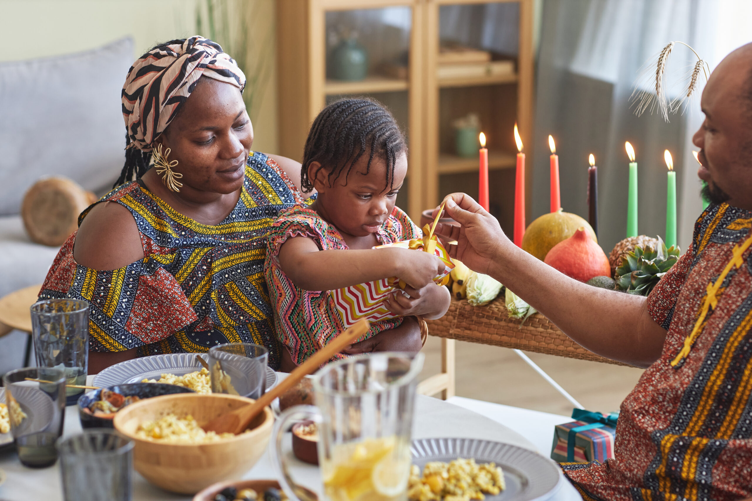 African little girl opening present together with her parents giving her for Kwanzaa holiday